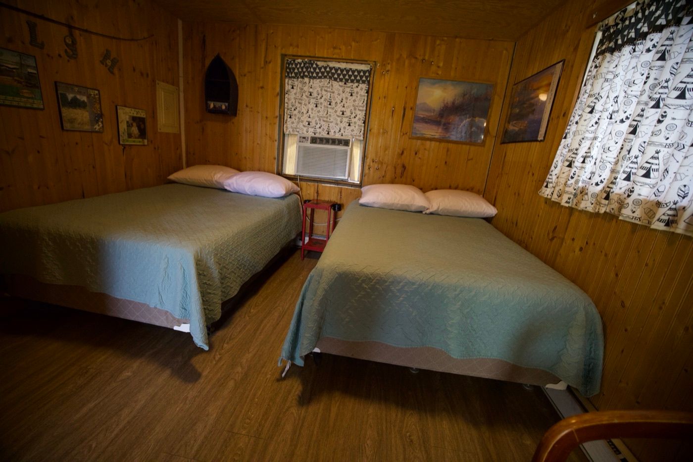 Wood-paneled cabin bedroom with two queen beds and a window air conditioner
