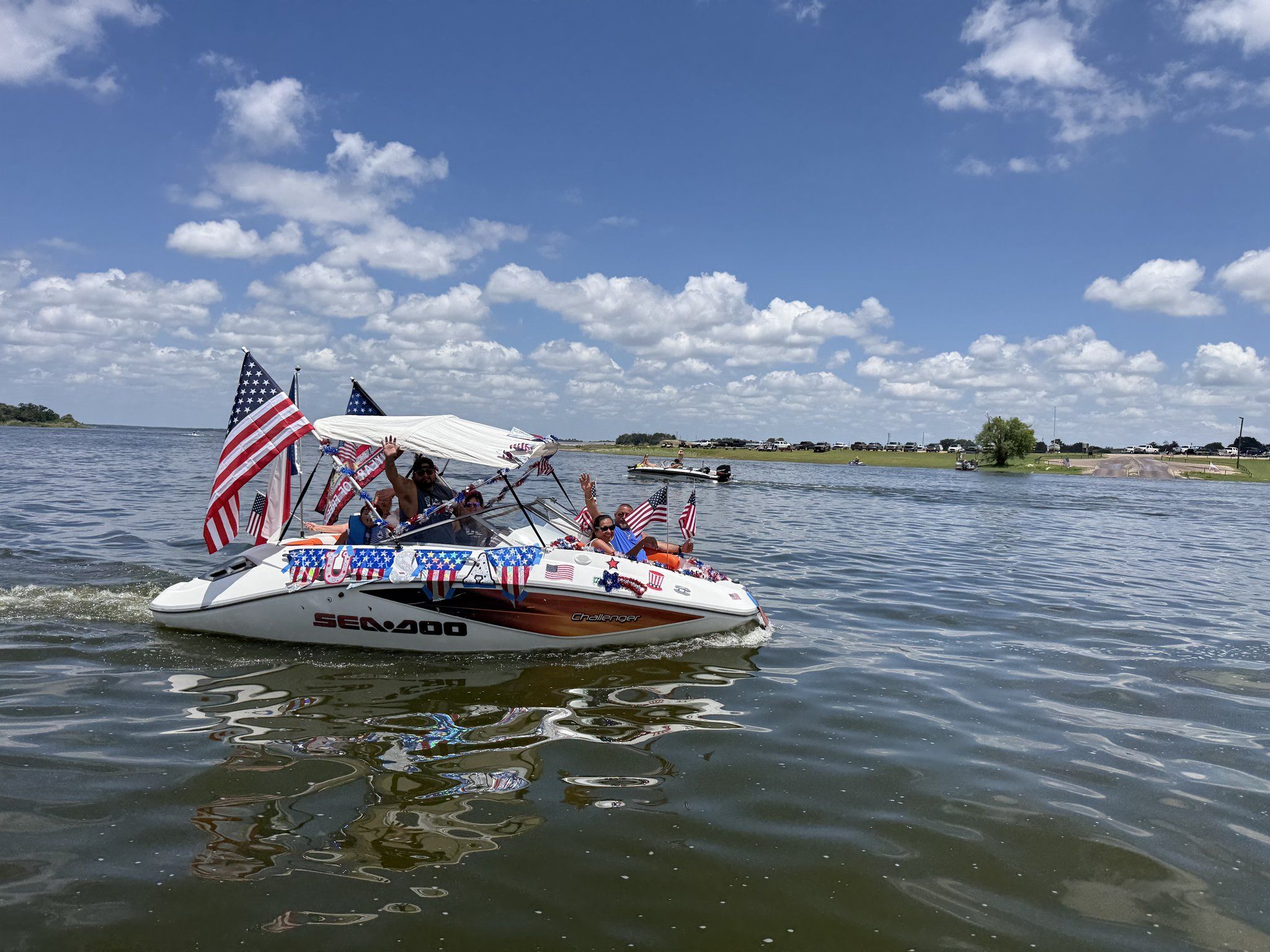 A white jet boat covered in American flags, bunting and streamers with passengers aboard, running in the holiday boat parade.