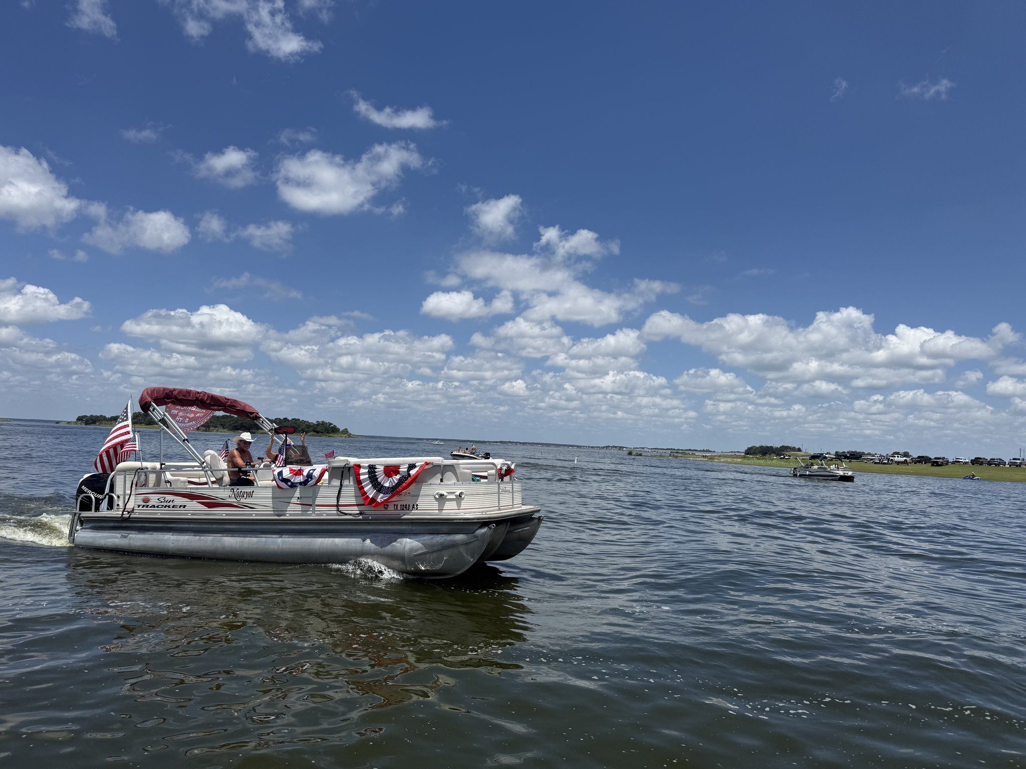 A pontoon boat trimmed with red, white and blue bunting cruising in a holiday boat parade.