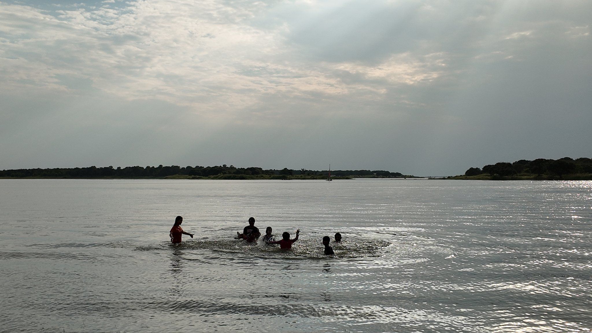 Adults and children silhouetted while swimming and splashing in the shallows under breaking sunbeams
