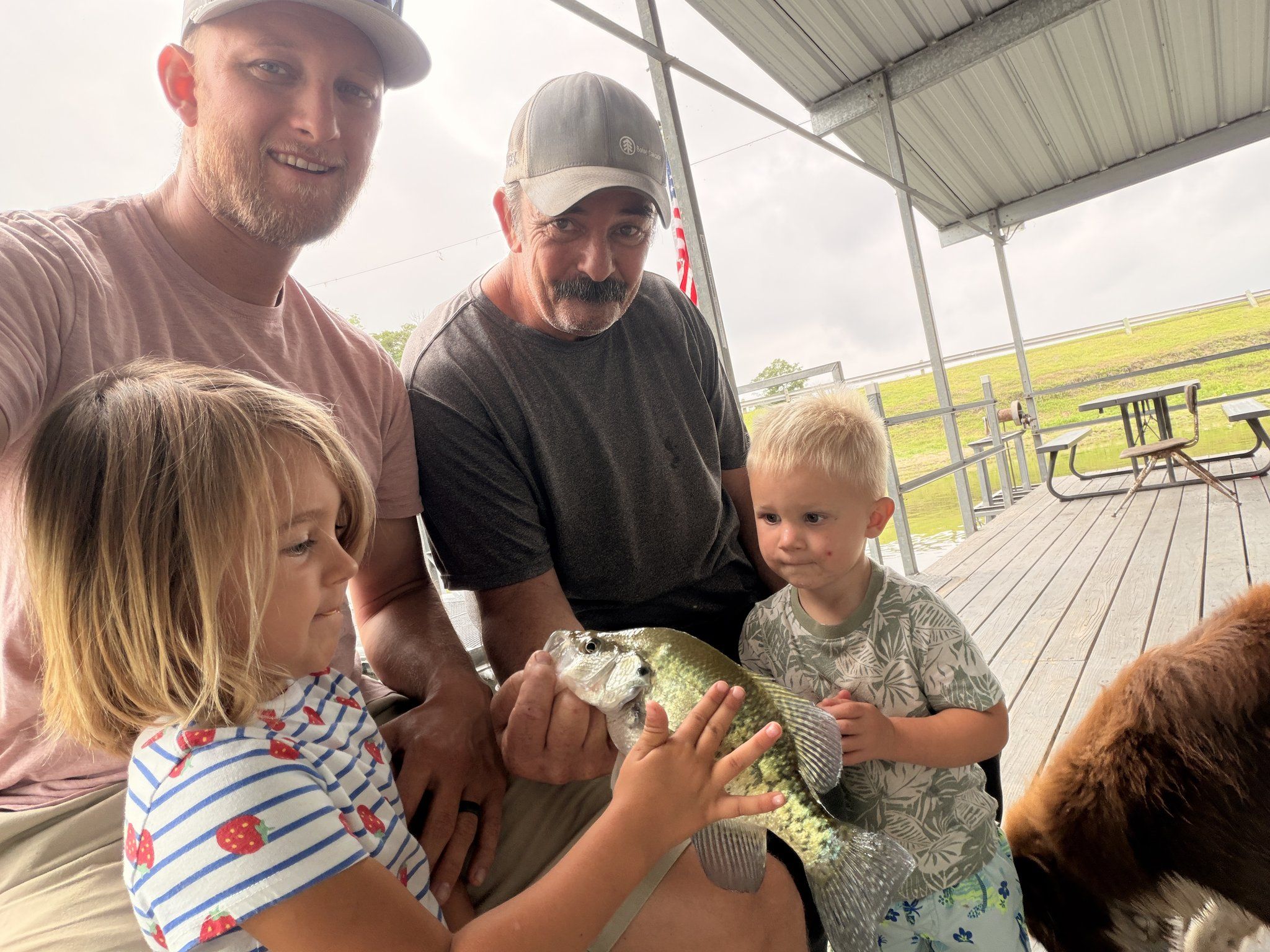 Two men and two small children proudly holding up a crappie they caught.