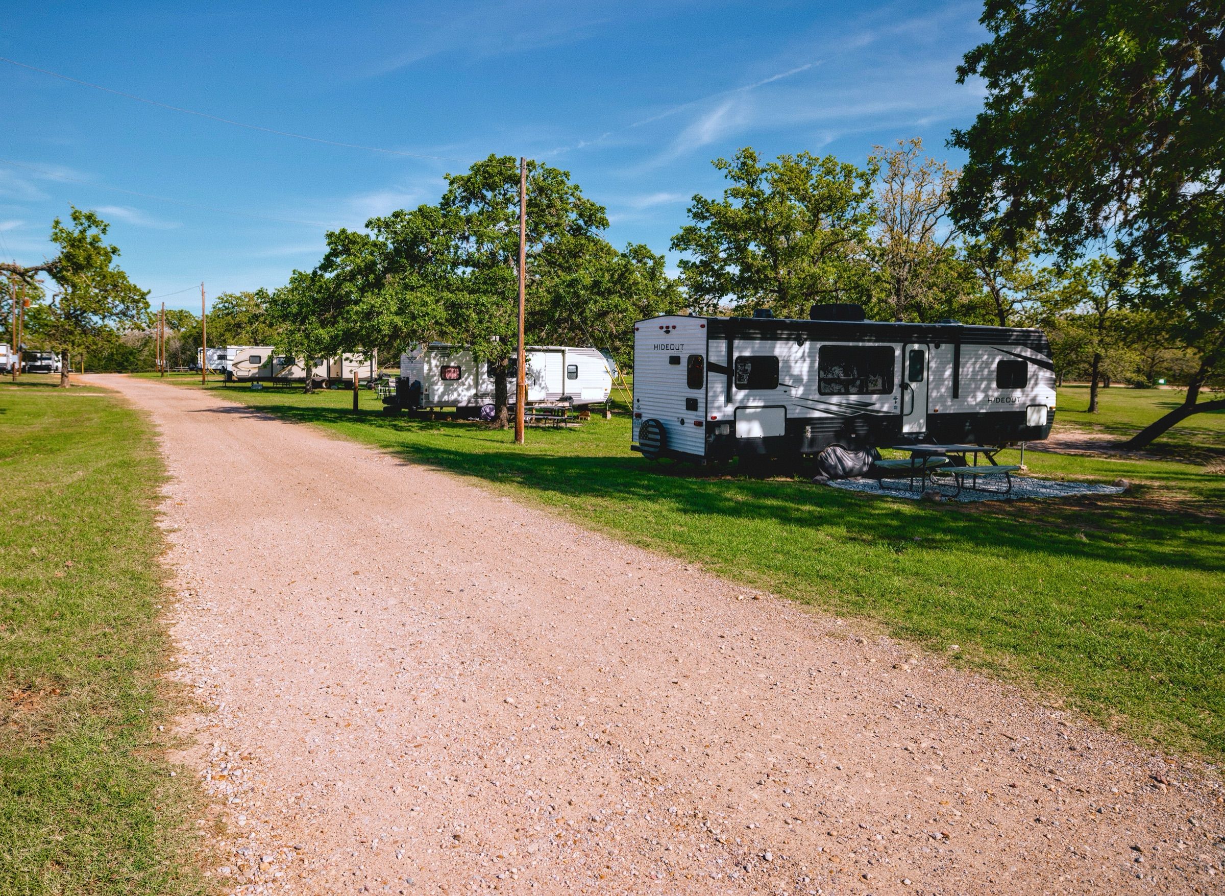 Gravel road lined with RV sites and oak trees under a blue sky at Overlook Park & Marina