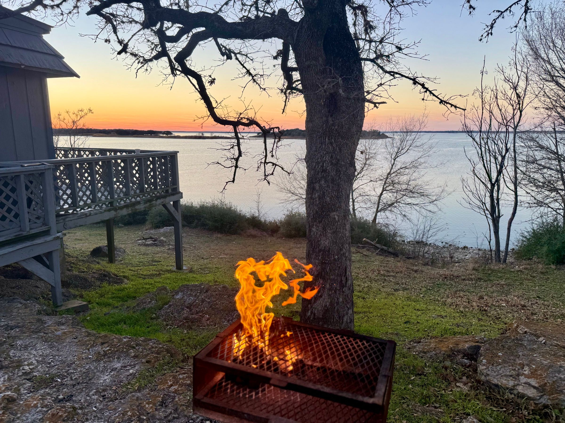 A campfire burning in a lakeside fire pit at sunset.