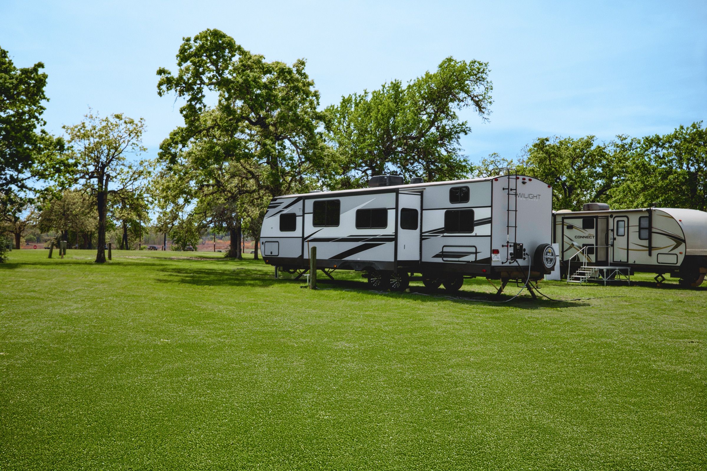 Travel trailers parked on green grass under shade oaks at an RV site.
