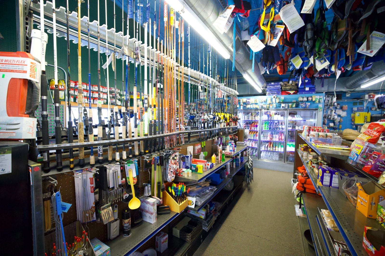 Inside the marina store: a wall of fishing rods and tackle, a drinks cooler, and life jackets hanging overhead.