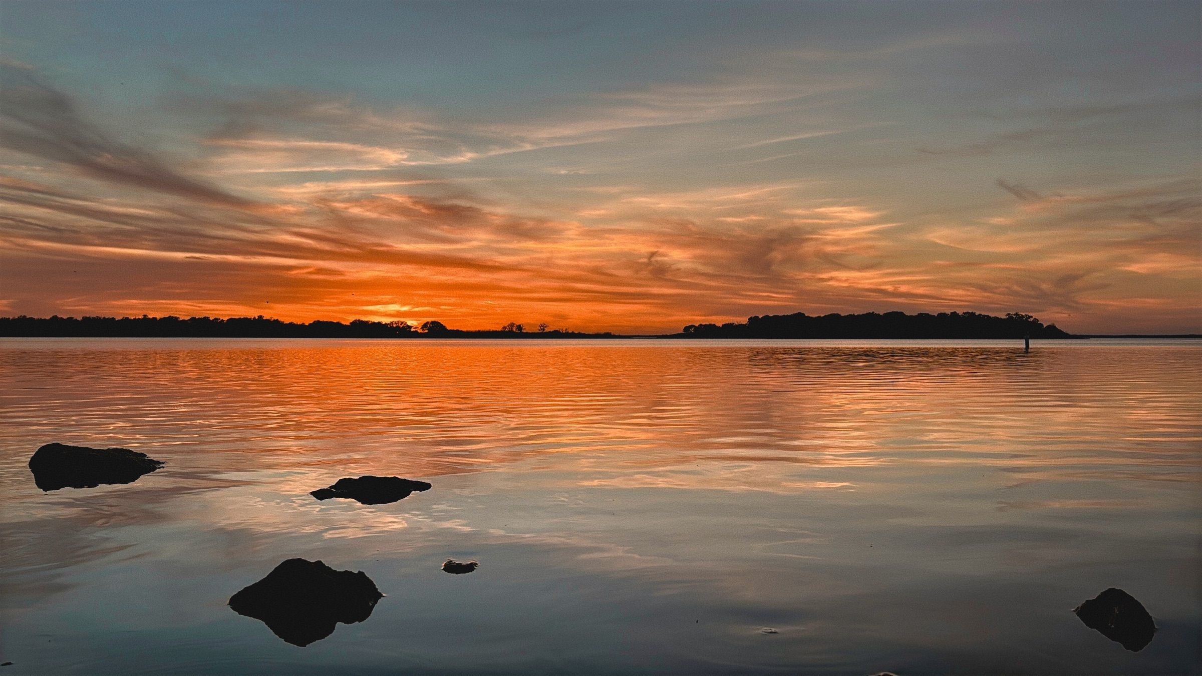 Vivid orange sunset over calm Lake Somerville, with dark rocks silhouetted in the water.
