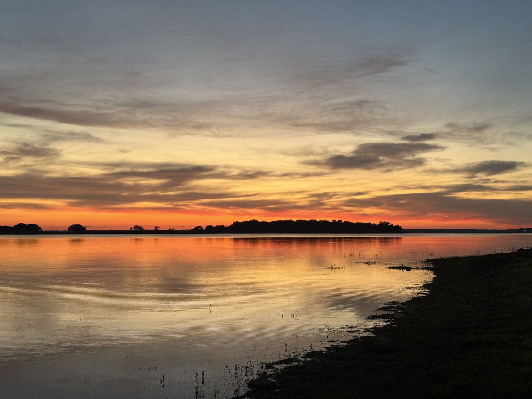 Orange and gold sunset light mirrored in still water beside a grassy bank on Lake Somerville