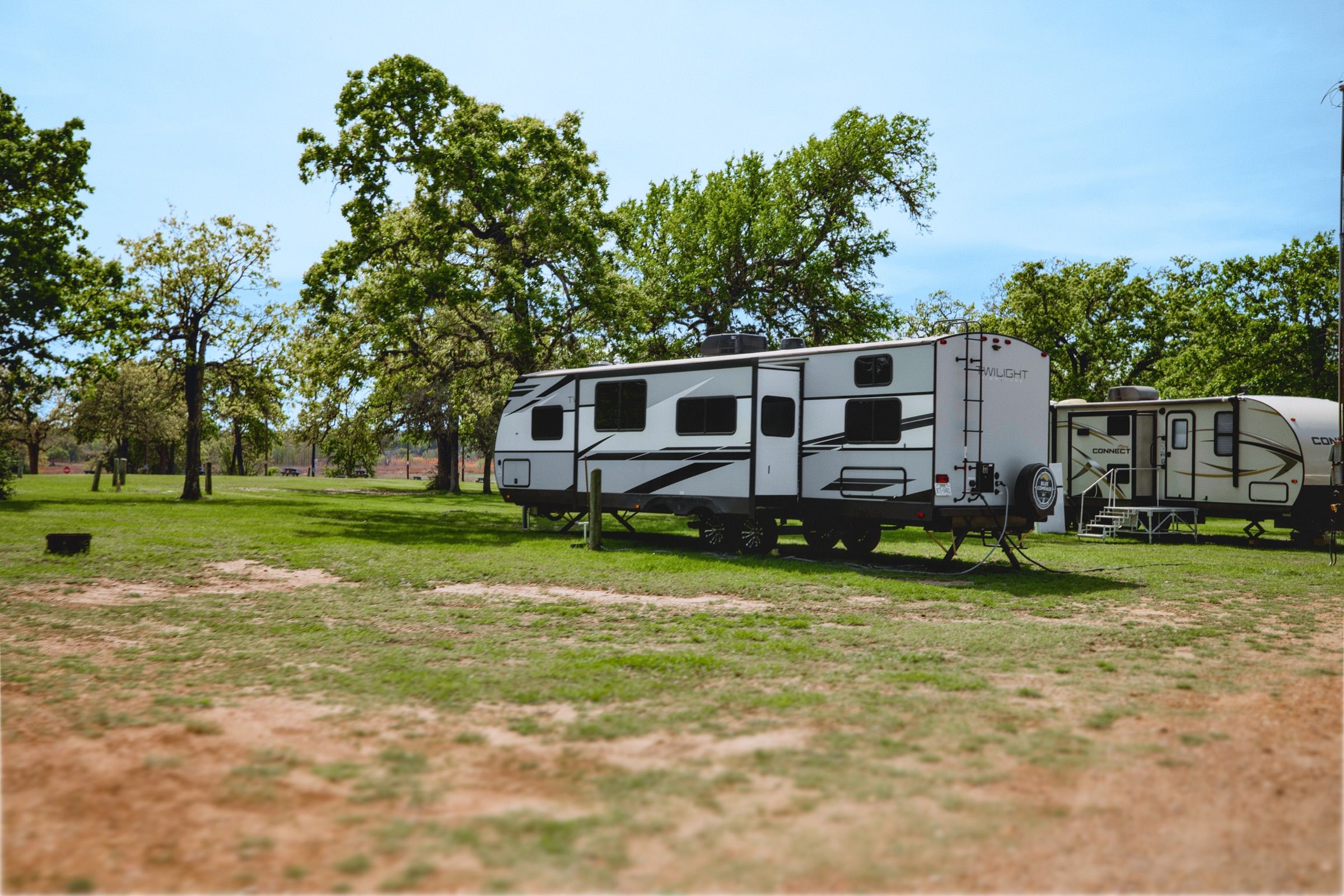 A travel trailer on a sunny green-grass RV site with trees behind it